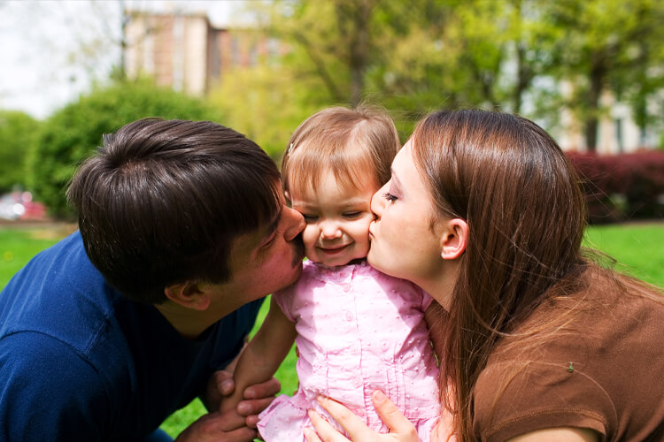 Mom and dad kissing baby outside